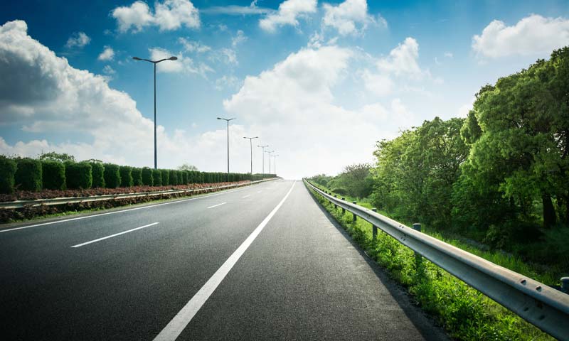 empty highway with trees lining both sides and blue sky in background